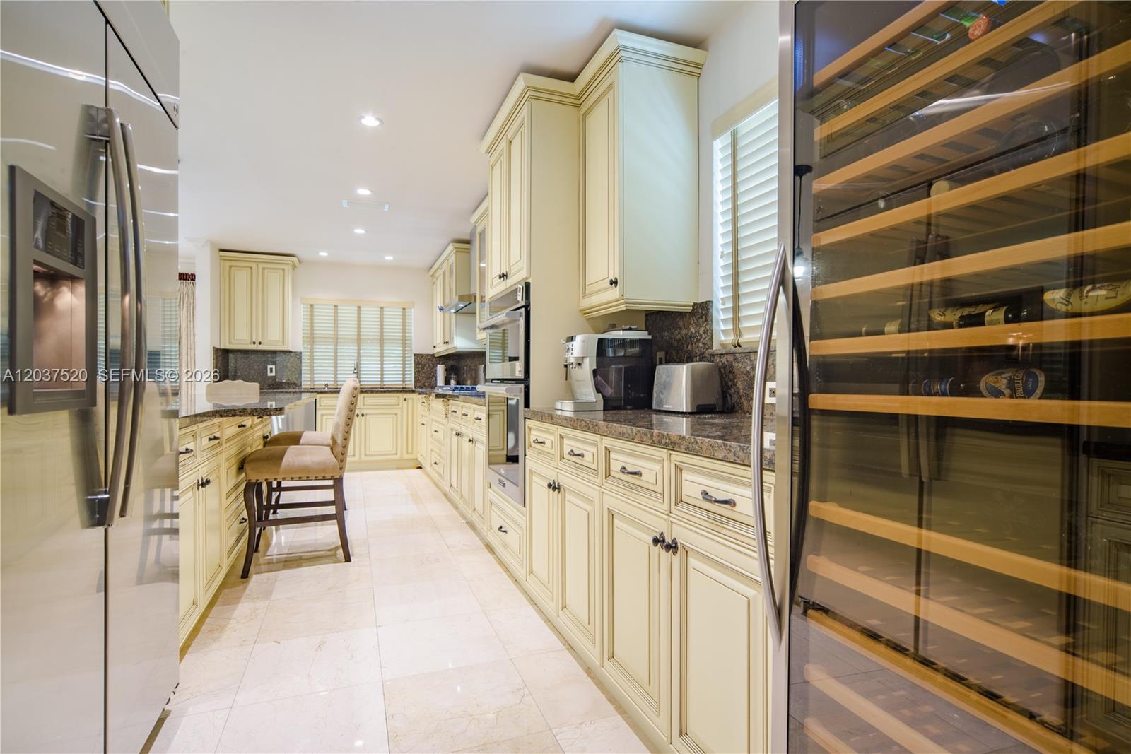 A kitchen features cream-colored cabinetry, granite countertops, stainless steel appliances, and a wine refrigerator — 3514 Crystal Ct, Miami FL 33133, MIAMI, FL