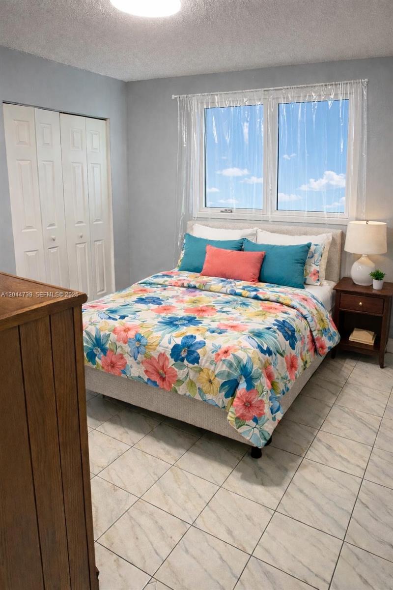 A bedroom features a floral bedspread, light gray walls, tile flooring, and a window — 10090 NW 80th Ct # 1540, Hialeah Gardens FL 33016, HIALEAH GARDENS, FL