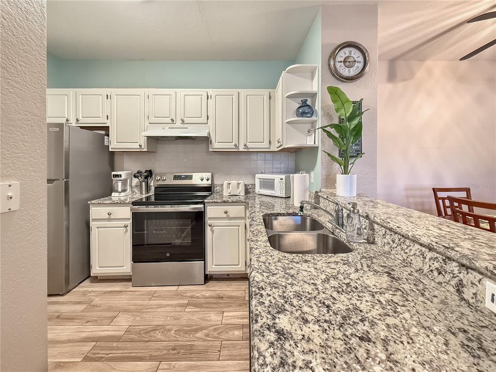 A kitchen features white cabinets, granite countertops, stainless steel appliances, and wood-look flooring — 8815 DUNES COURT UNIT 105, KISSIMMEE, FL