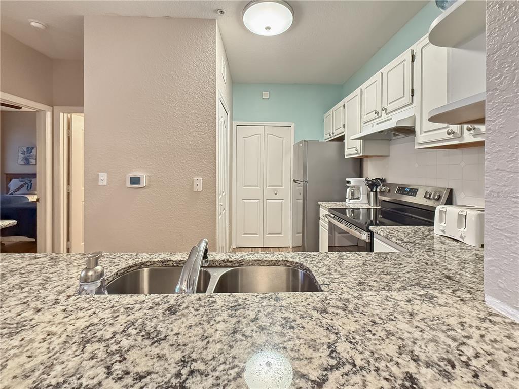 A kitchen features granite countertops, white cabinets, stainless steel appliances, and a double-basin sink — 8815 DUNES COURT UNIT 105, KISSIMMEE, FL