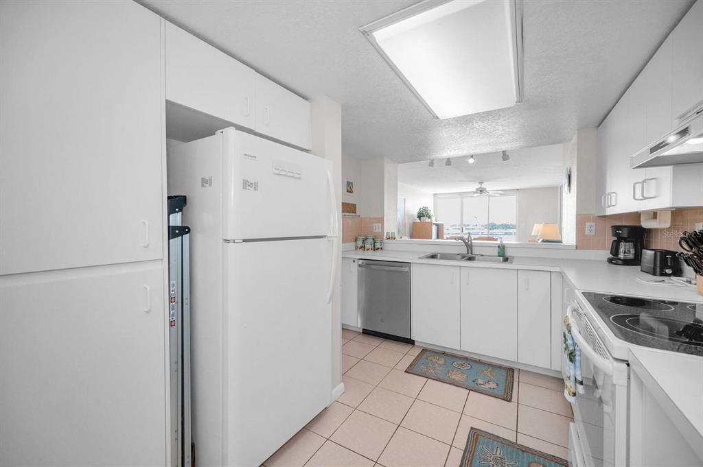 A white kitchen features tile flooring, white cabinetry, and a pass-through window to the living area — 6085 BAHIA DEL MAR CIRCLE UNIT 467, ST PETERSBURG, FL