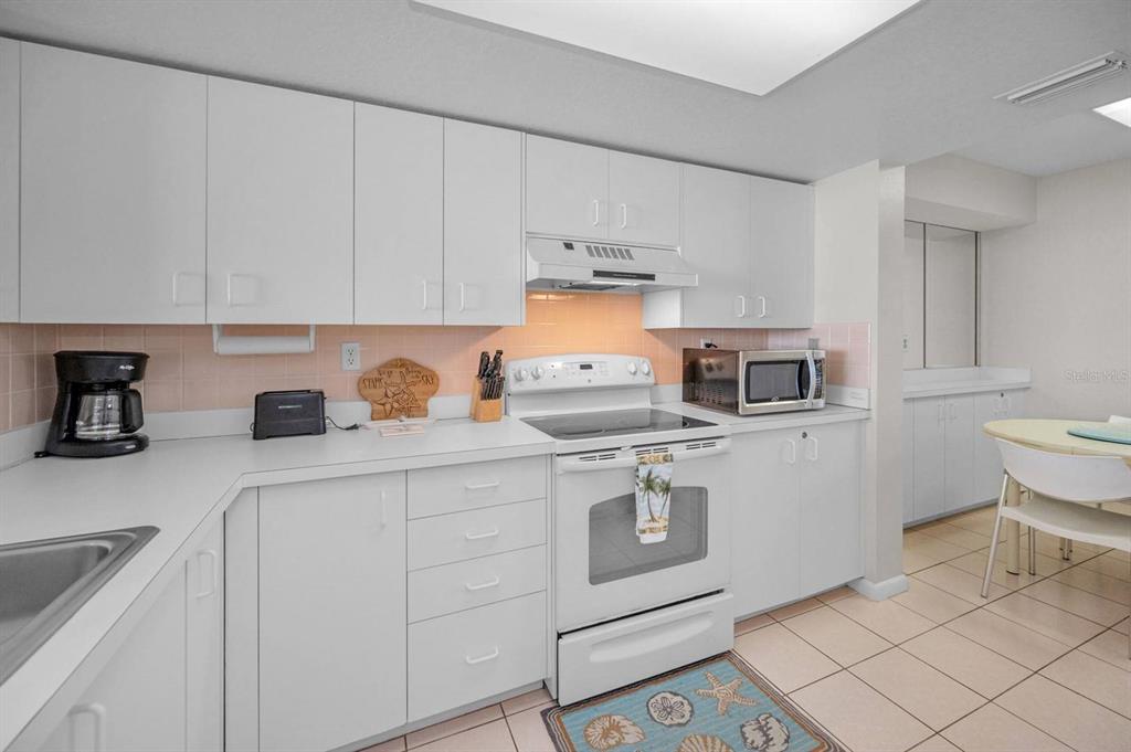 A kitchen features white cabinets, white appliances, a light-colored tile floor, and a backsplash — 6085 BAHIA DEL MAR CIRCLE UNIT 467, ST PETERSBURG, FL