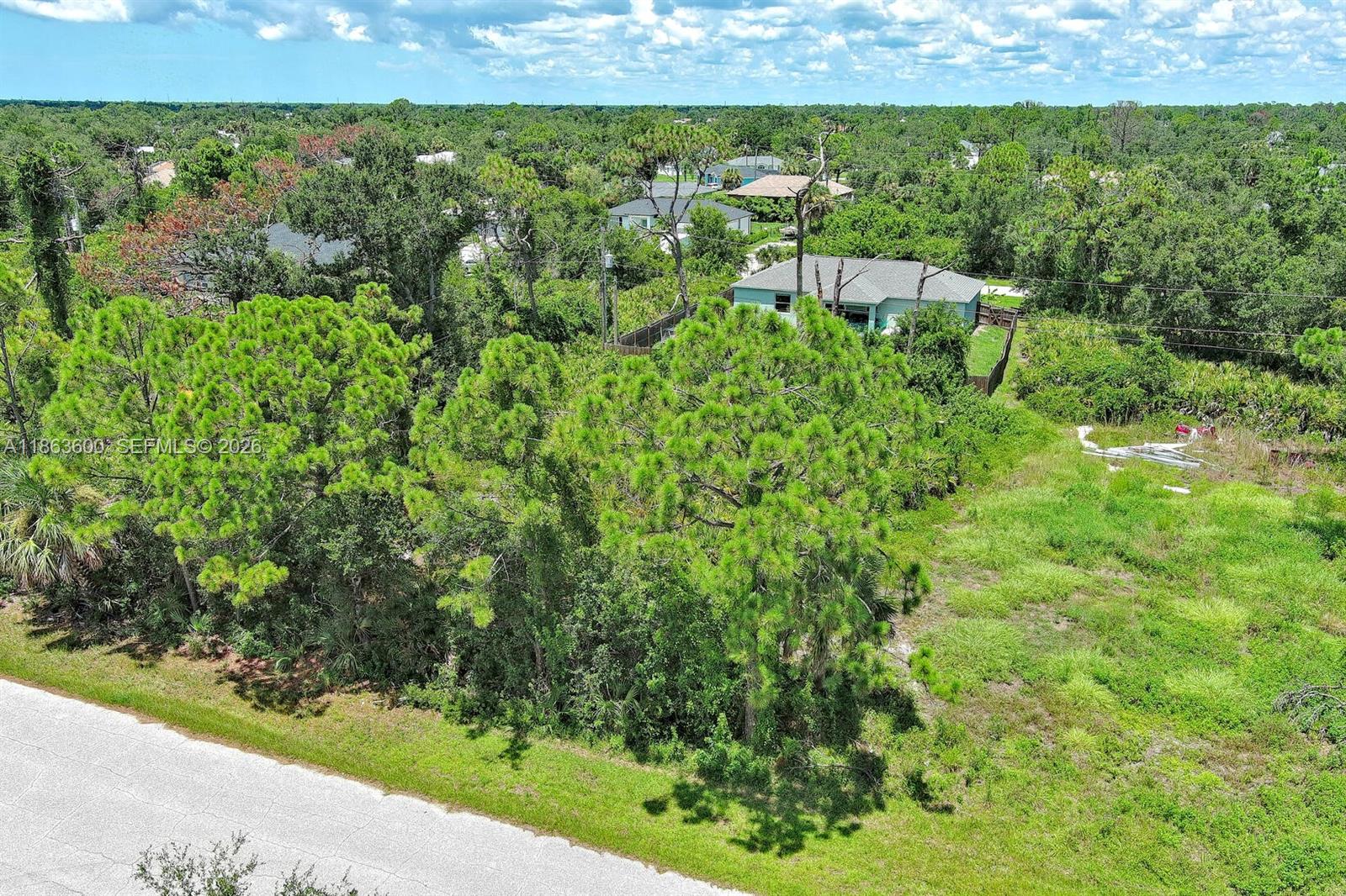 An aerial view shows a vacant grassy lot with trees next to a residential house — 11944 Brookside Ave, Port Charlotte FL 33981, PORT CHARLOTTE, FL