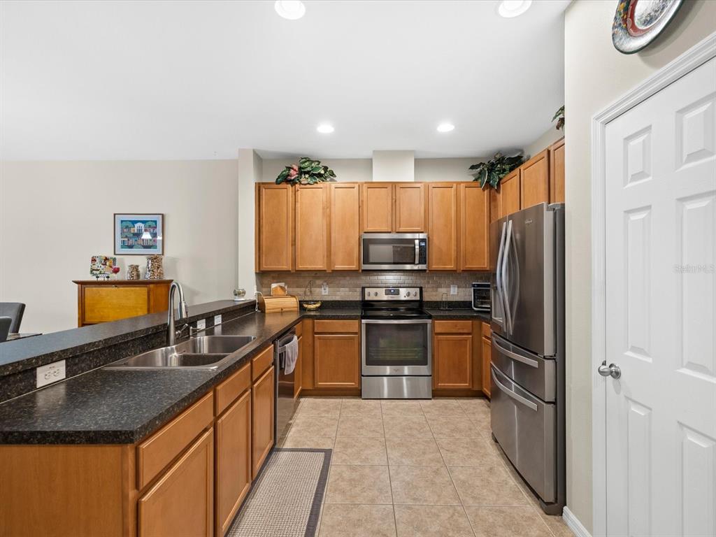 A kitchen with wood cabinets, dark countertops, stainless steel appliances, and tile flooring — 2239 BARRACUDA COURT, HOLIDAY, FL