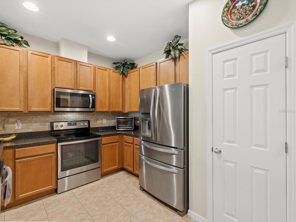 A kitchen features wood cabinets, stainless steel appliances, a tile floor, and a pantry door — 2239 BARRACUDA COURT, HOLIDAY, FL