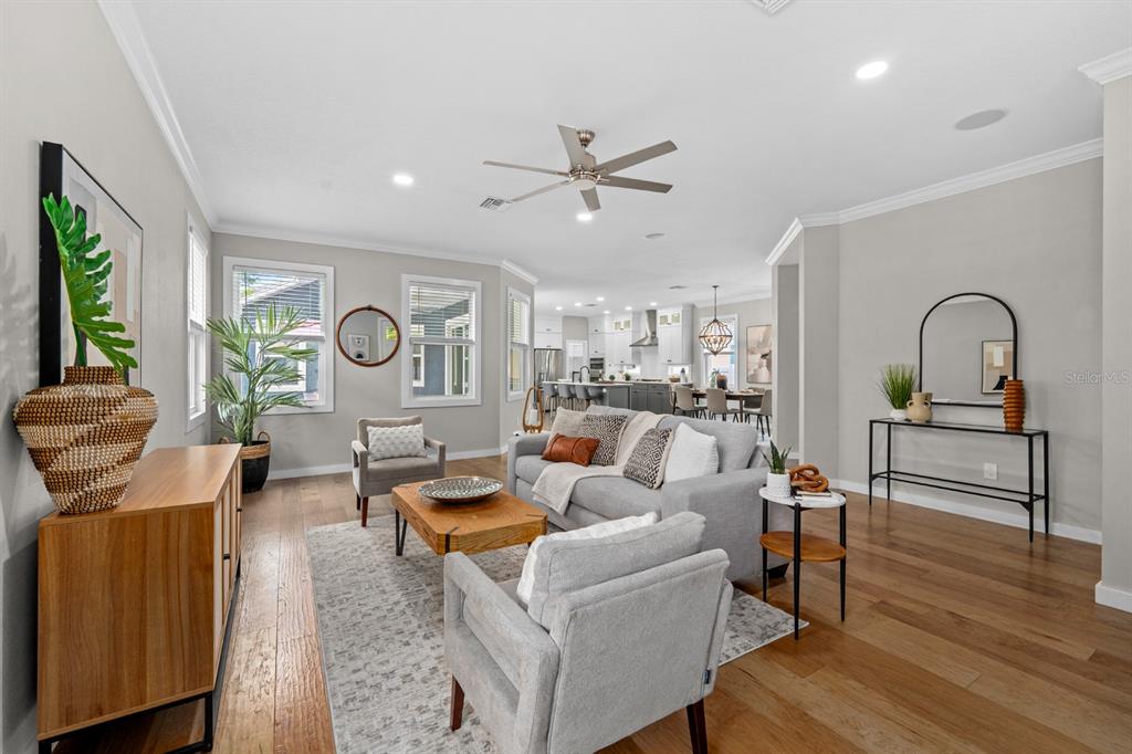 A bright, open-concept living room features hardwood floors, a gray sofa, and a modern kitchen — 1028 5TH STREET N, ST PETERSBURG, FL