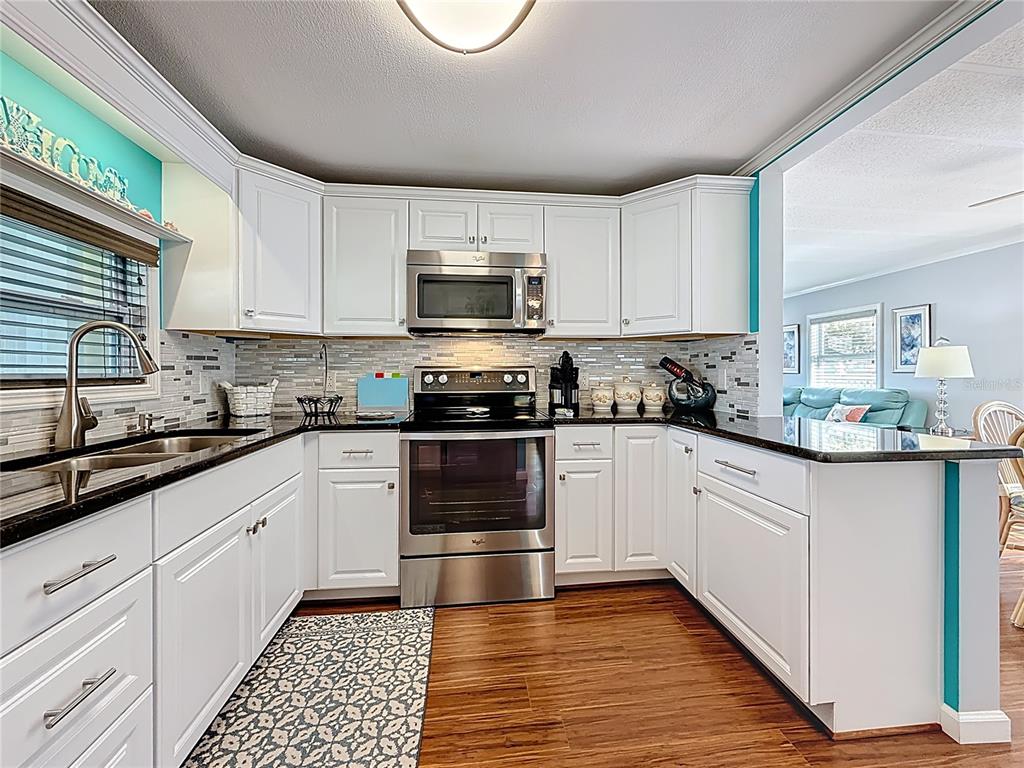 A kitchen features white cabinets, stainless steel appliances, black countertops, and a tile backsplash — 7880 54TH AVENUE N UNIT 54, ST PETERSBURG, FL