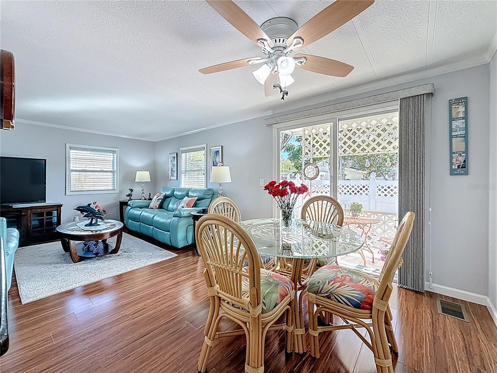A living and dining room with wood floors, a ceiling fan, and a glass-topped table — 7880 54TH AVENUE N UNIT 54, ST PETERSBURG, FL