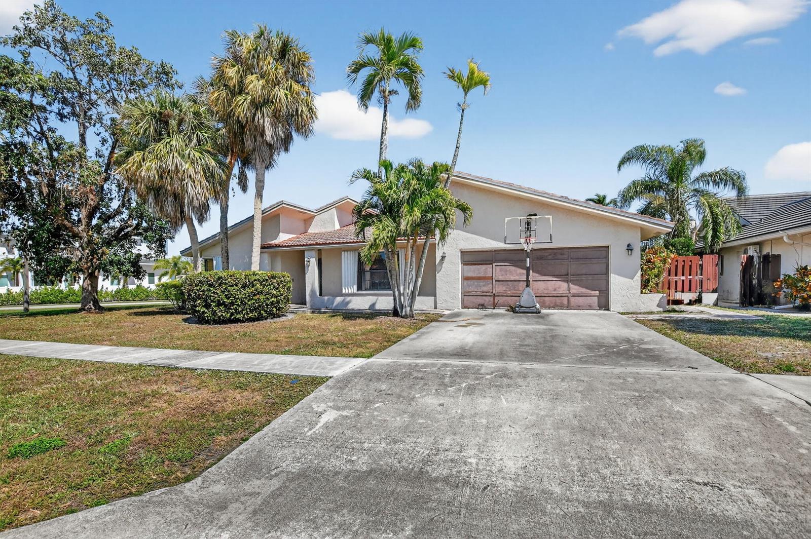 A single-story house with a concrete driveway, basketball hoop, and palm trees in the front — 22220 Morning Glory Terrace, Boca Raton FL 33433, BOCA RATON, FL