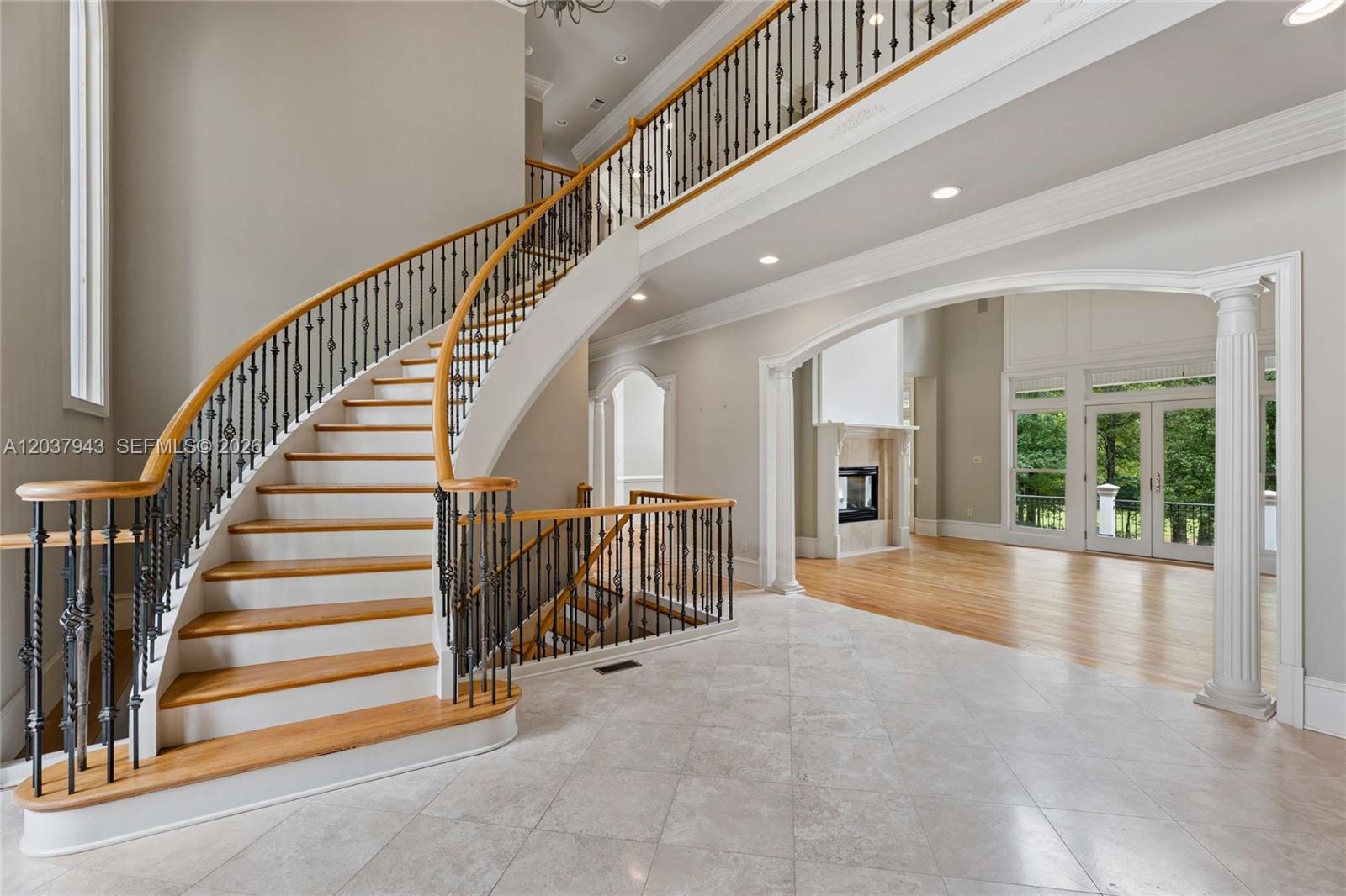 A grand foyer features a curved wooden staircase with iron railings and light tile flooring — 1845 Kathy Whitworth Drive, GA 30517, GA