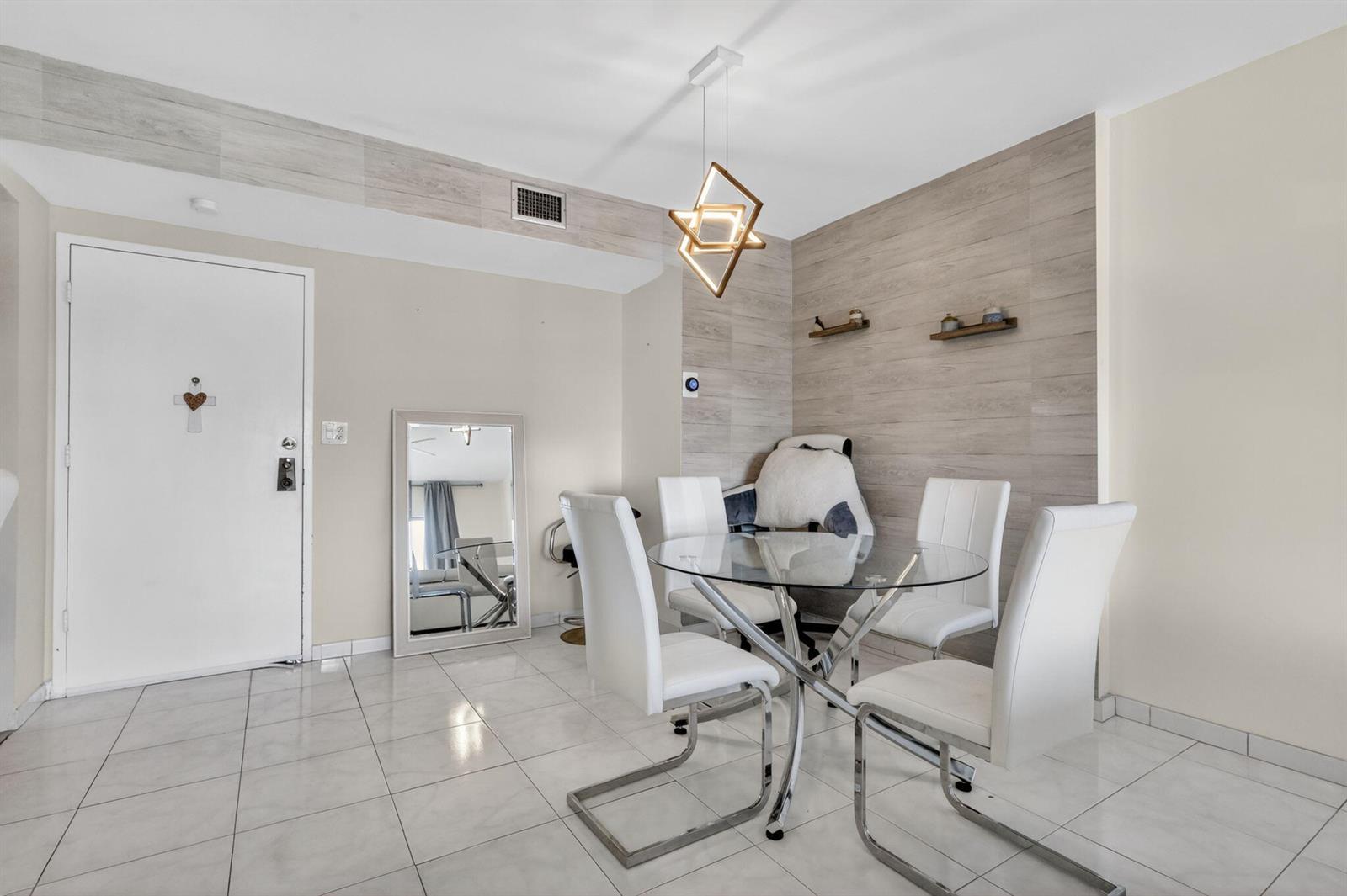 A dining area features a glass table, four white chairs, and a geometric pendant light — 4330 Hillcrest Drive # 302, Hollywood FL 33021, HOLLYWOOD, FL