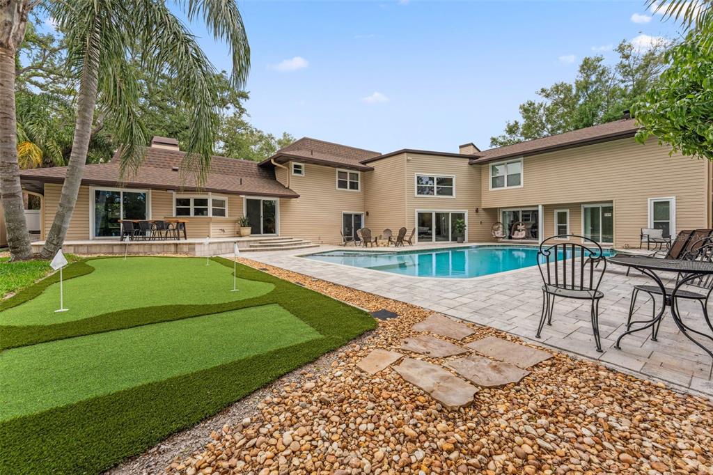A stone fire pit with Adirondack chairs sits on a patio beside a swimming pool — 1584 OAK LANE, CLEARWATER, FL
