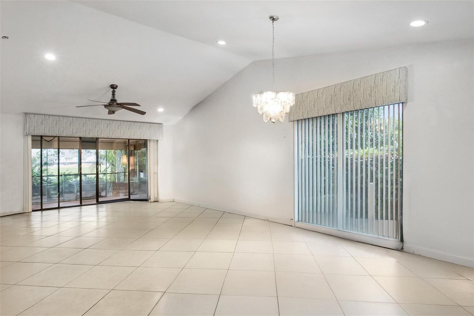 A bright, empty room with vaulted ceilings, tile floors, a chandelier, and large sliding doors — 16131 Laurel Drive # 33, Weston FL 33326, WESTON, FL