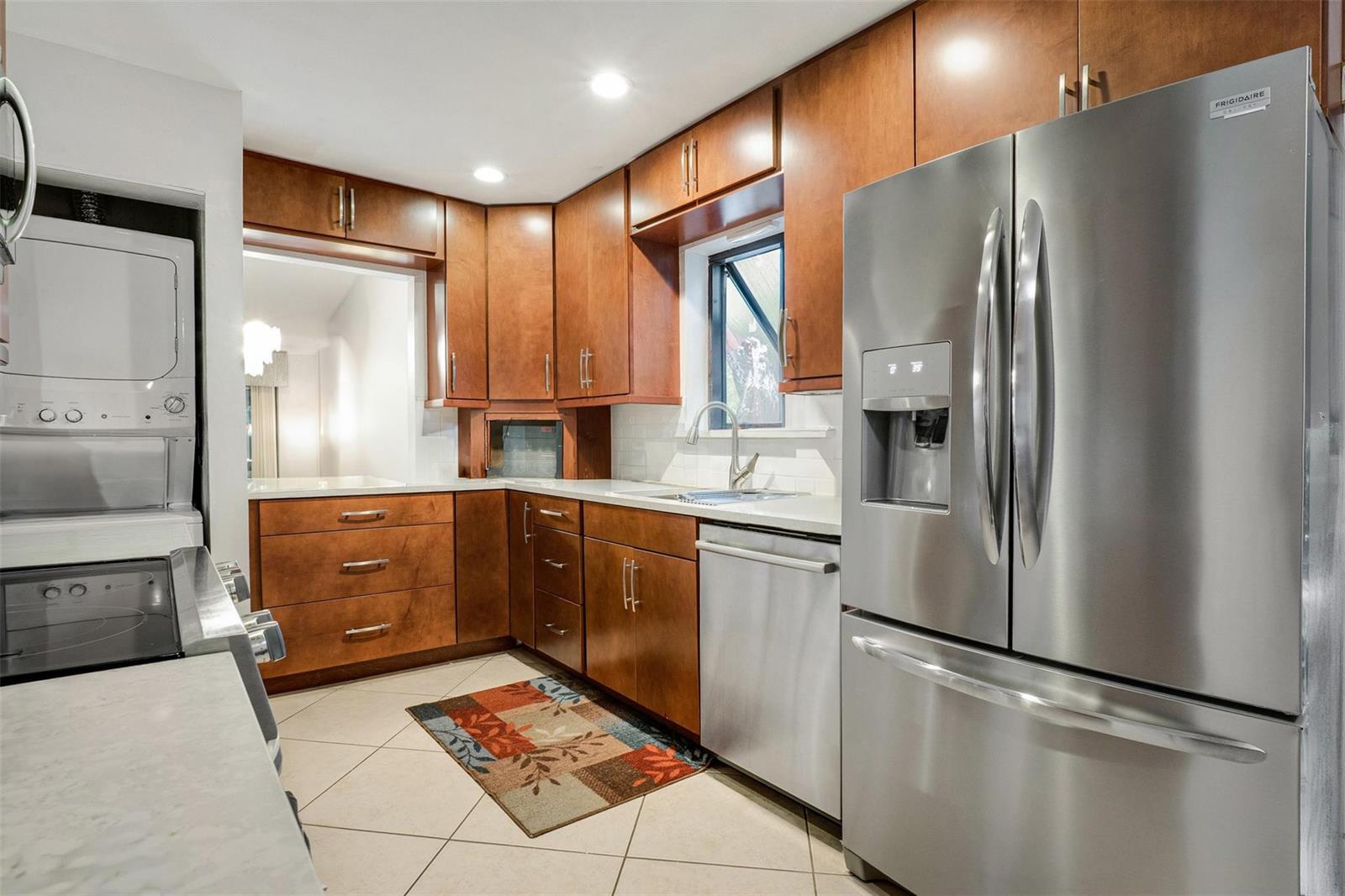 A kitchen with wood cabinets, stainless steel appliances, white countertops, and a stacked laundry unit — 16131 Laurel Drive # 33, Weston FL 33326, WESTON, FL