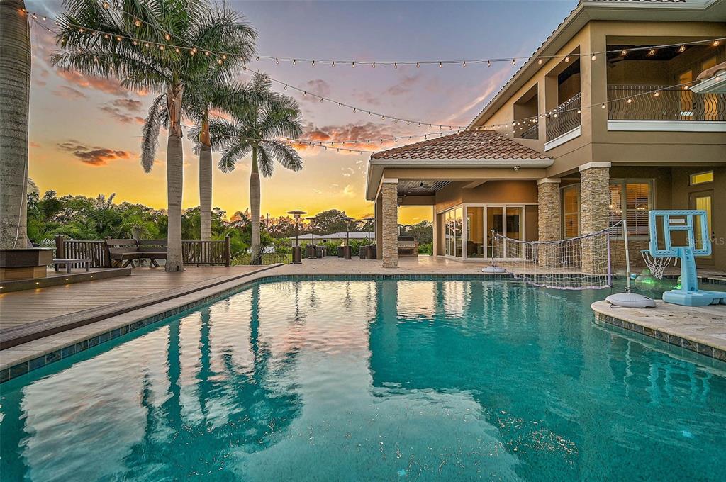 A backyard swimming pool with a basketball hoop and string lights at sunset — 6722 HAWKINS ROAD, SARASOTA, FL