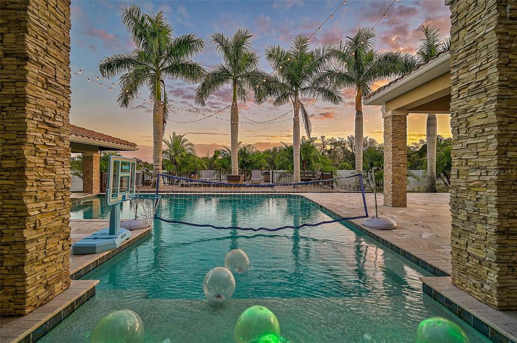 A swimming pool with a volleyball net and basketball hoop sits on a stone patio — 6722 HAWKINS ROAD, SARASOTA, FL