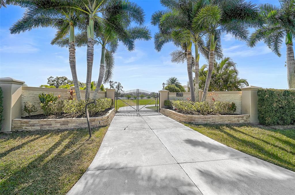 A concrete driveway leads to a gated entrance flanked by stone walls and palm trees — 6722 HAWKINS ROAD, SARASOTA, FL