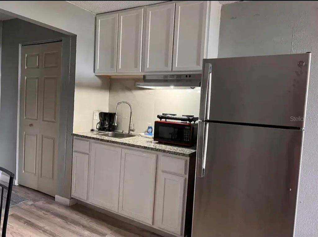 A small kitchen features light gray cabinets, granite countertops, a stainless steel refrigerator, and sink — 43420 HIGHWAY 27 UNIT 425, DAVENPORT, FL