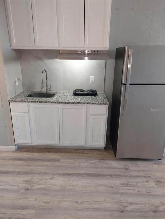A small kitchen features white cabinets, a granite countertop, a stainless refrigerator, and wood flooring — 43420 HIGHWAY 27 UNIT 425, DAVENPORT, FL
