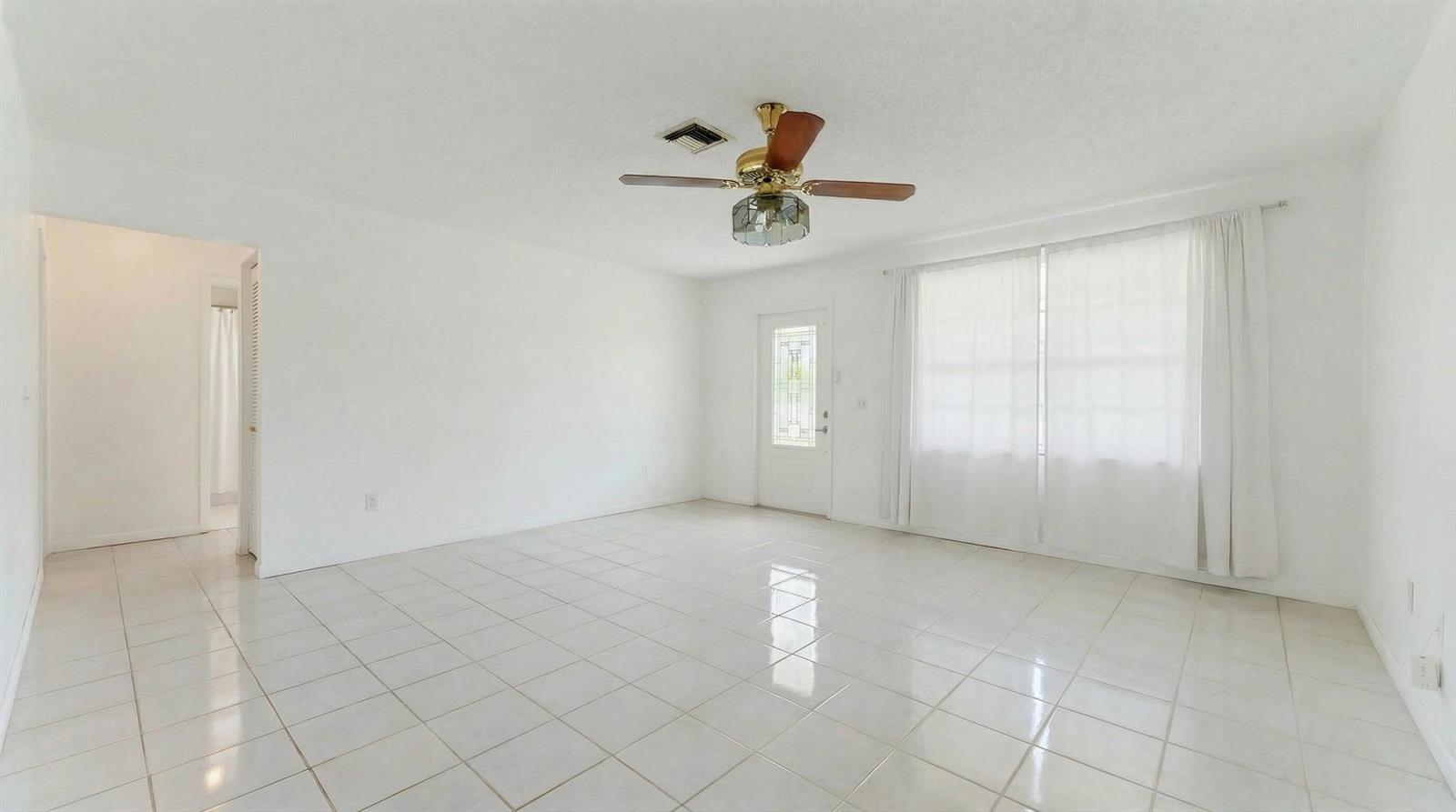 A bright, empty living room features white tile floors, a ceiling fan, and large windows — 428 Alemeda Drive, Palm Springs FL 33461, PALM SPRINGS, FL