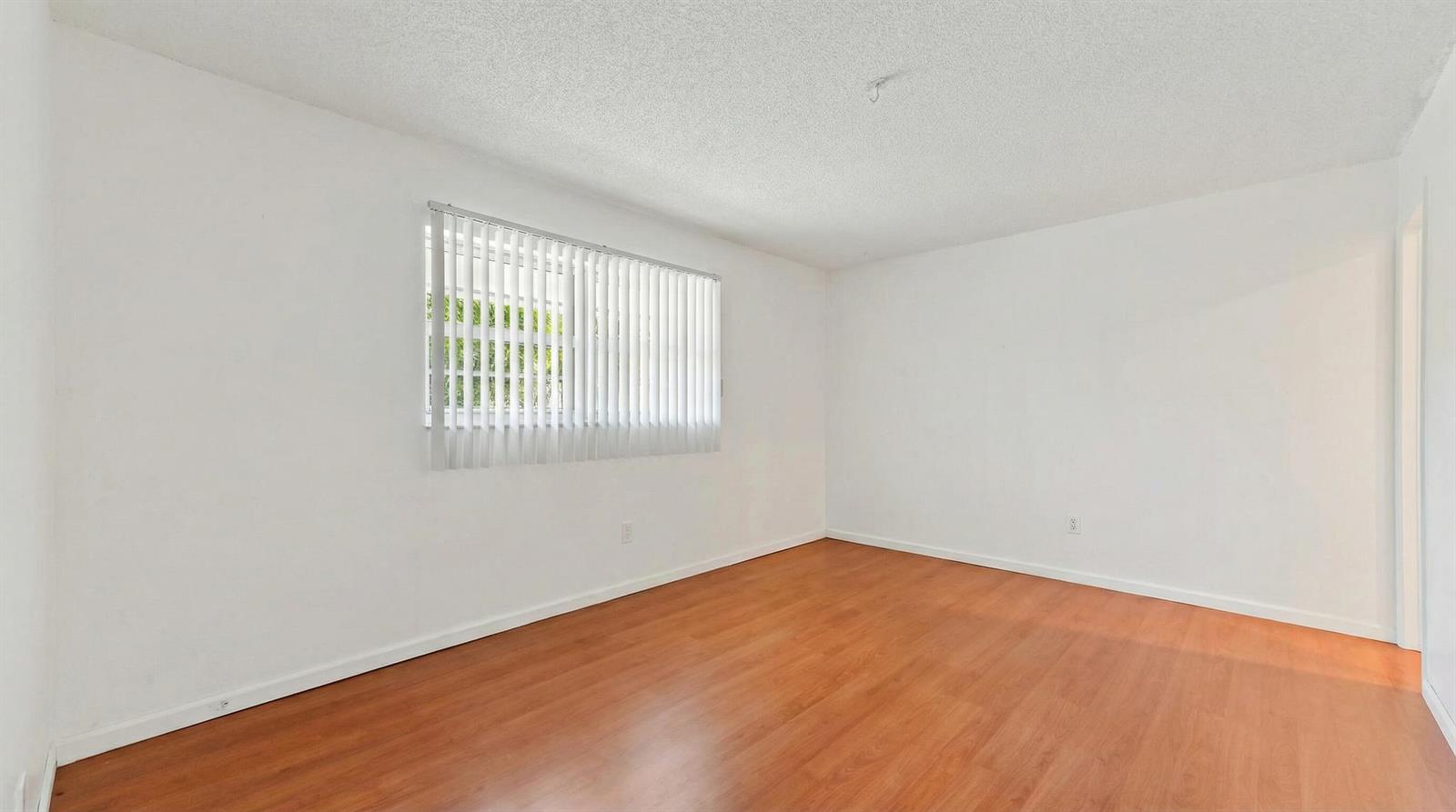 An empty room features white walls, wood-look flooring, and a window with vertical blinds — 428 Alemeda Drive, Palm Springs FL 33461, PALM SPRINGS, FL