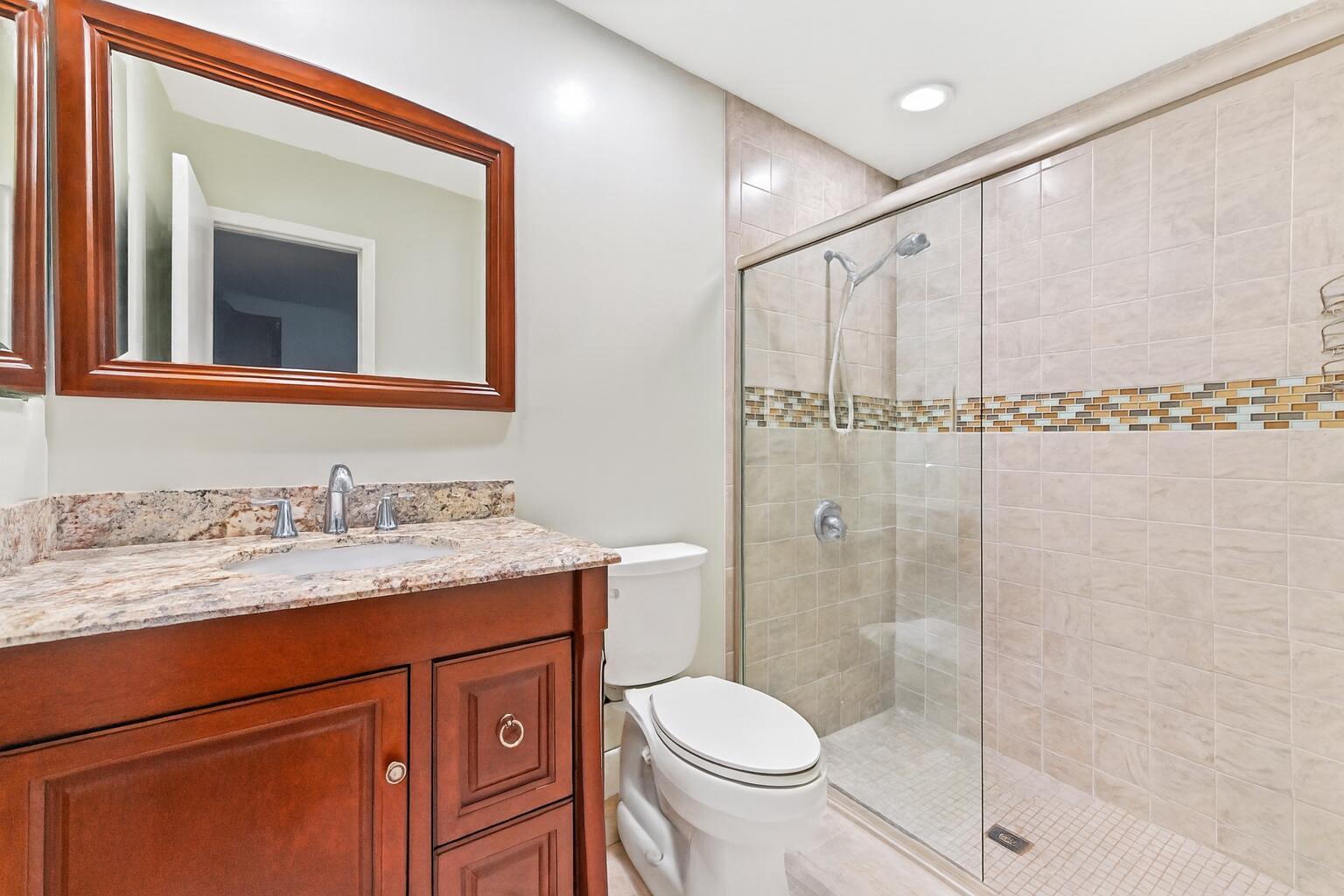 A bathroom features a wood vanity with a granite countertop, toilet, and glass-enclosed shower — 428 Alemeda Drive, Palm Springs FL 33461, PALM SPRINGS, FL