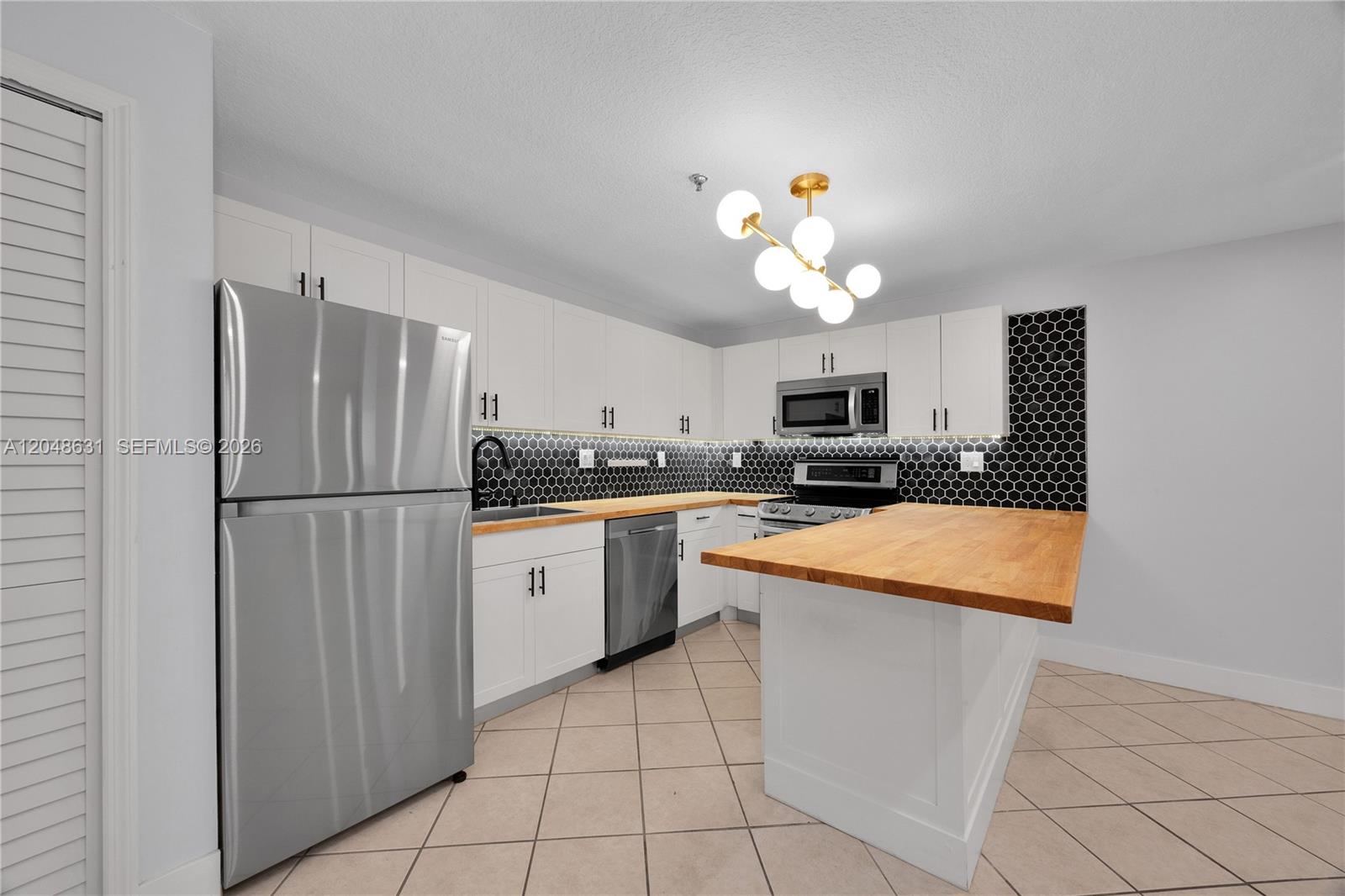 A kitchen features white cabinets, stainless steel appliances, a wood countertop, and black hexagonal tiles — 2734 Bird Ave # 301, Miami FL 33133, MIAMI, FL