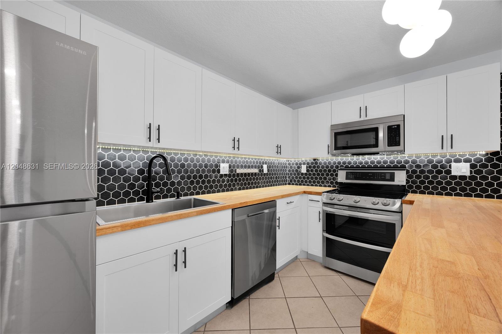 A kitchen features white cabinets, a black honeycomb backsplash, stainless steel appliances, and wood countertops — 2734 Bird Ave # 301, Miami FL 33133, MIAMI, FL