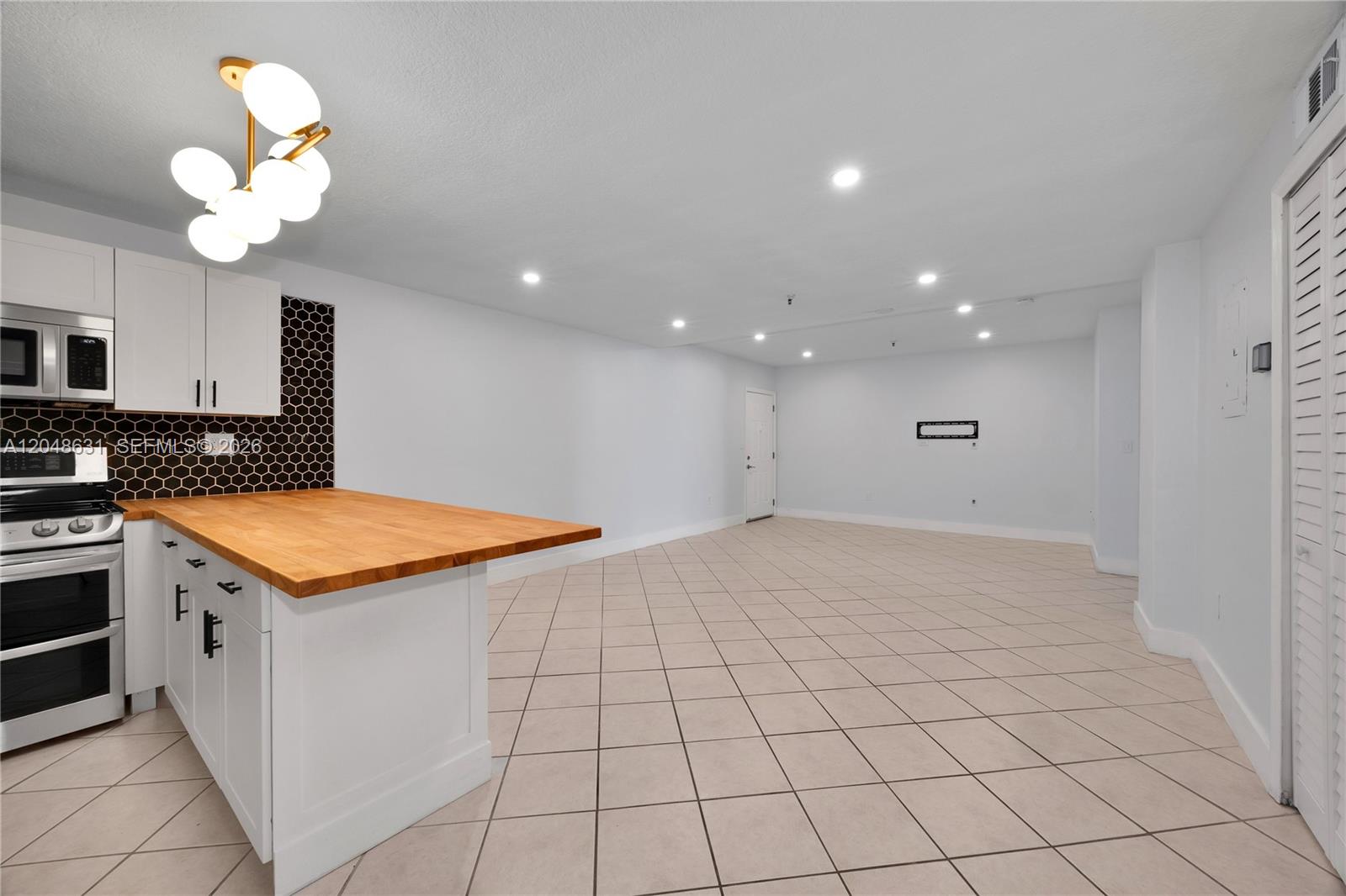 A kitchen with white cabinets and a wood countertop opens into a large tiled room — 2734 Bird Ave # 301, Miami FL 33133, MIAMI, FL