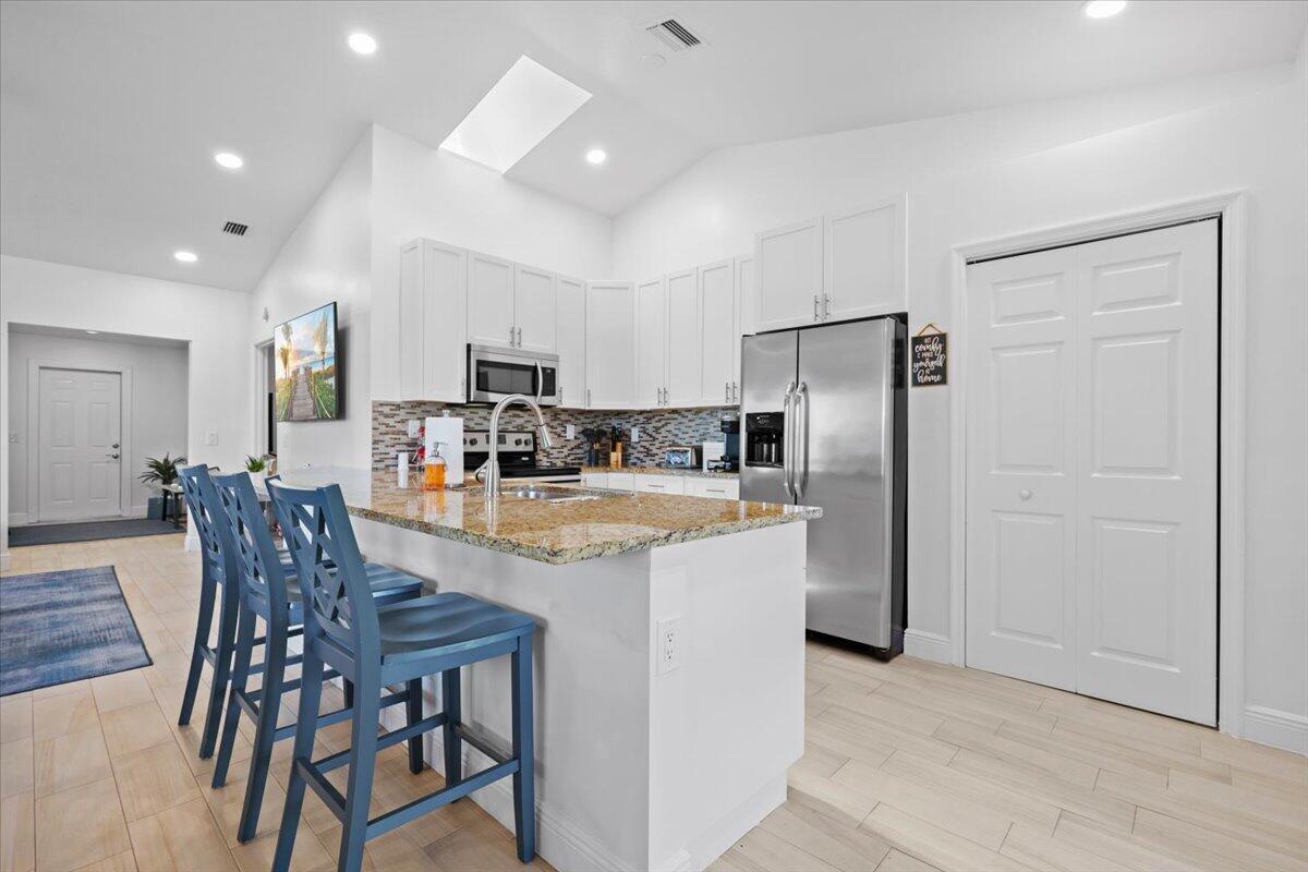 A kitchen features white cabinetry, granite countertops, a stainless steel refrigerator, and blue bar stools — 6077 Francis Street, Jupiter FL 33458, JUPITER, FL