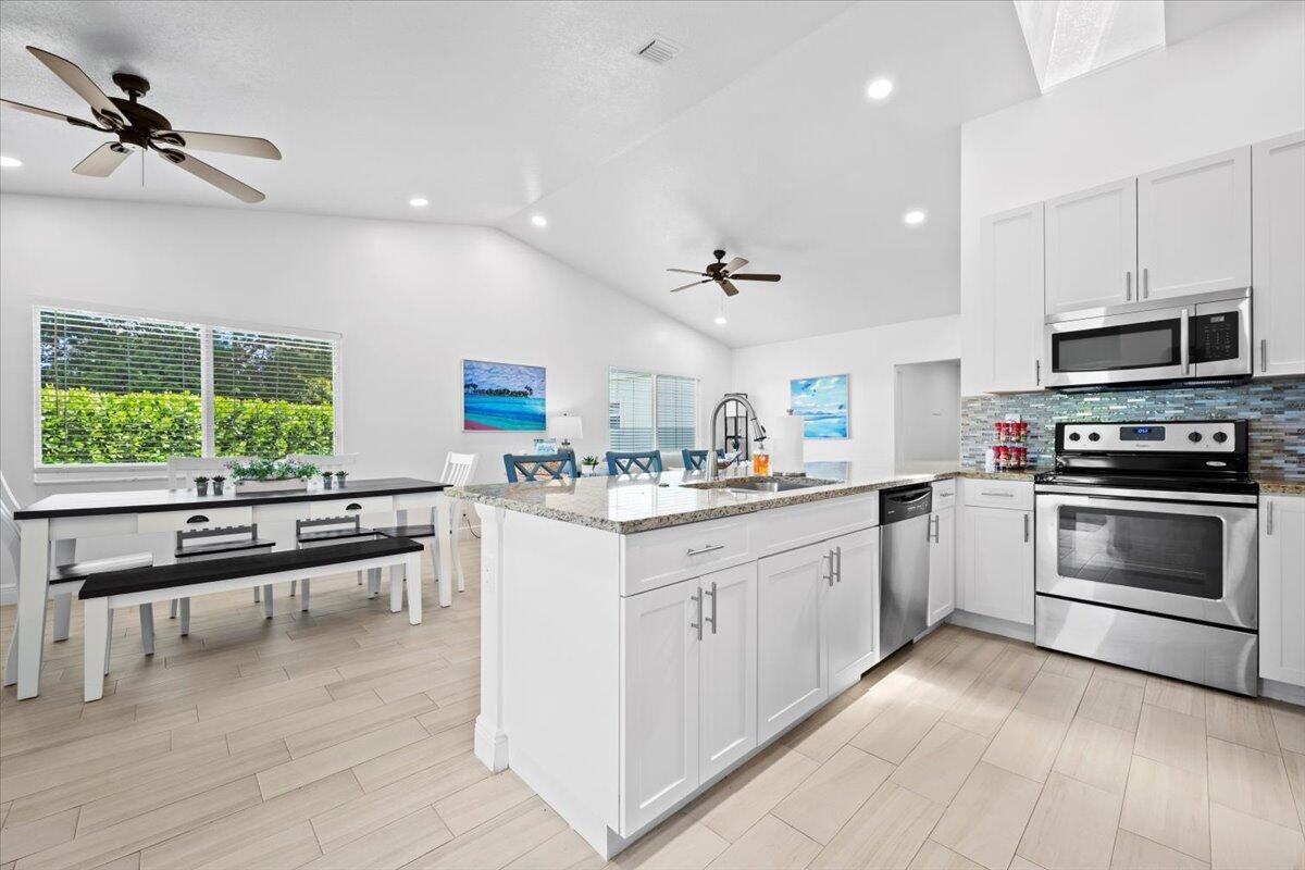 A kitchen with white cabinets, granite countertops, and a dining area with a bench — 6077 Francis Street, Jupiter FL 33458, JUPITER, FL