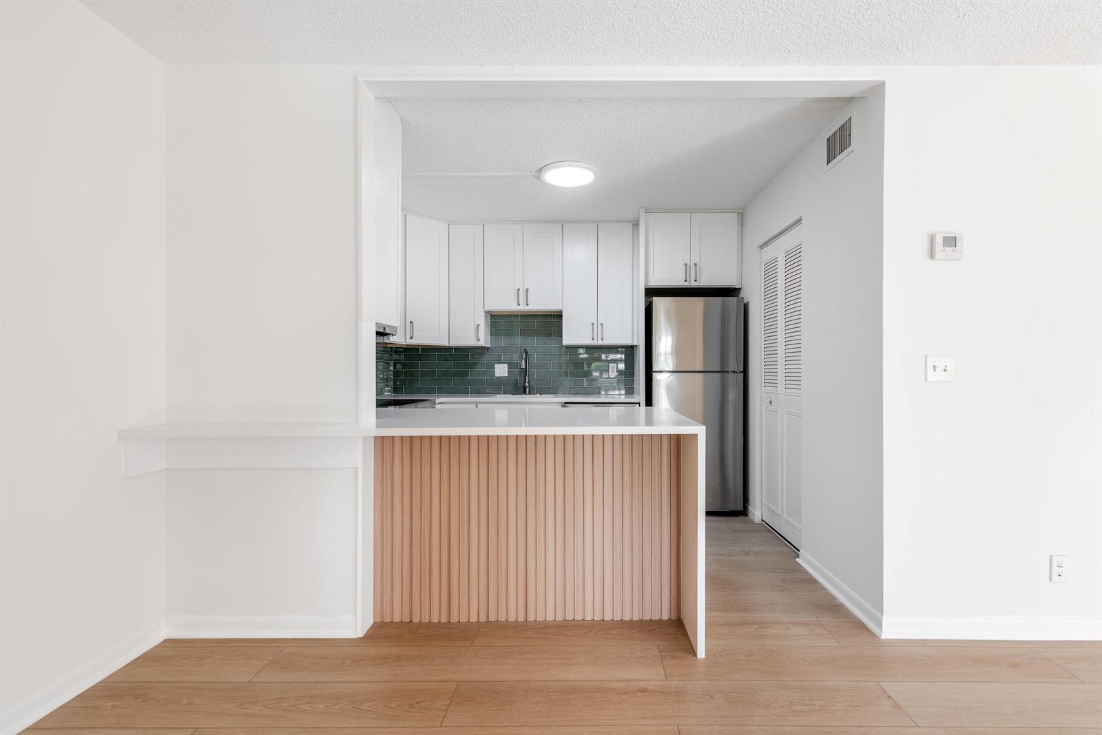 A kitchen with white cabinets, a green tile backsplash, and a wood-slatted breakfast bar — 3561 Tall Pine Way # 2, FL 33463, FL
