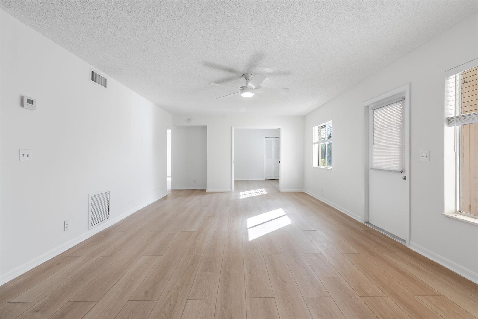 An empty room features white walls, light wood-look flooring, a ceiling fan, and a door — 3561 Tall Pine Way # 2, FL 33463, FL