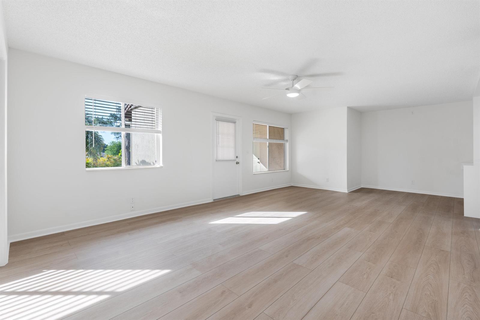 An empty living room features white walls, light wood-look flooring, a ceiling fan, and windows — 3561 Tall Pine Way # 2, FL 33463, FL