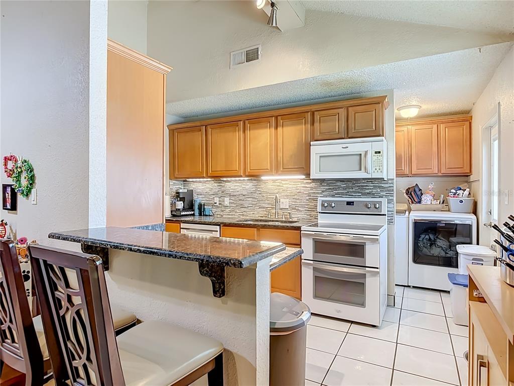 A kitchen features wood cabinets, white appliances, a tiled backsplash, and a breakfast bar — 1123 W HANCOCK DRIVE, DELTONA, FL