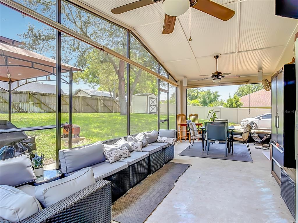 A screened-in patio features a long wicker sofa, dining set, and ceiling fans — 1123 W HANCOCK DRIVE, DELTONA, FL
