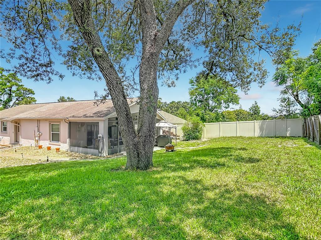 A grassy backyard features a large oak tree, a screened-in patio, and a vinyl privacy fence — 1123 W HANCOCK DRIVE, DELTONA, FL