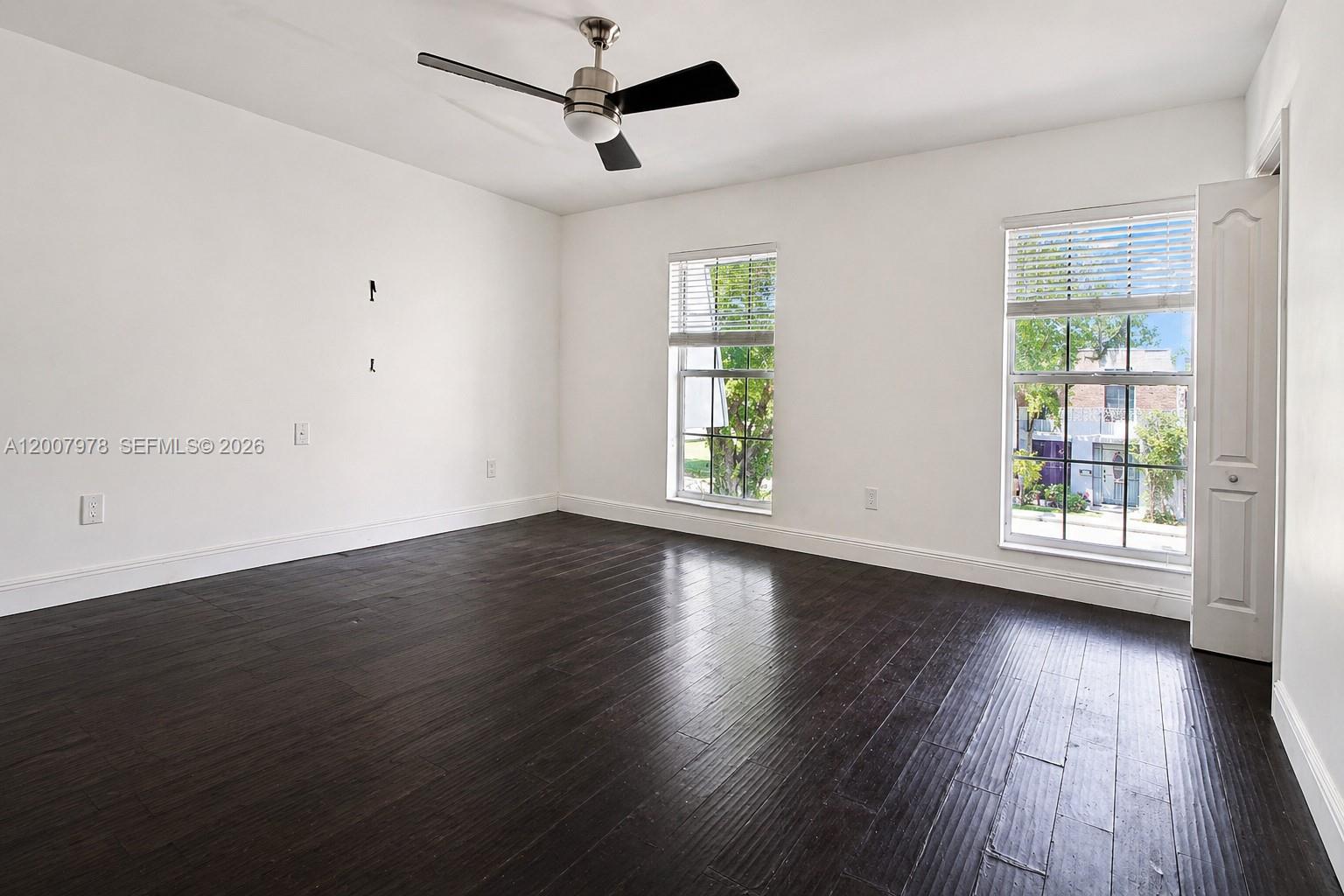 An empty bedroom features dark wood flooring, white walls, a ceiling fan, and two windows — 13501 NE 23rd Ct, North Miami FL 33181, NORTH MIAMI, FL