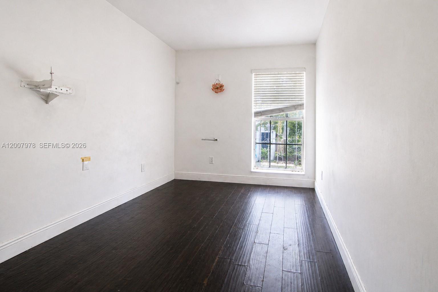 An empty room features dark wood flooring, white walls, and a single window with blinds — 13501 NE 23rd Ct, North Miami FL 33181, NORTH MIAMI, FL
