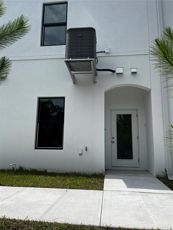 The exterior of a white building features a wall-mounted air conditioning unit and a doorway — 4363 CAMBIO GARDENS COURT, TAMPA, FL