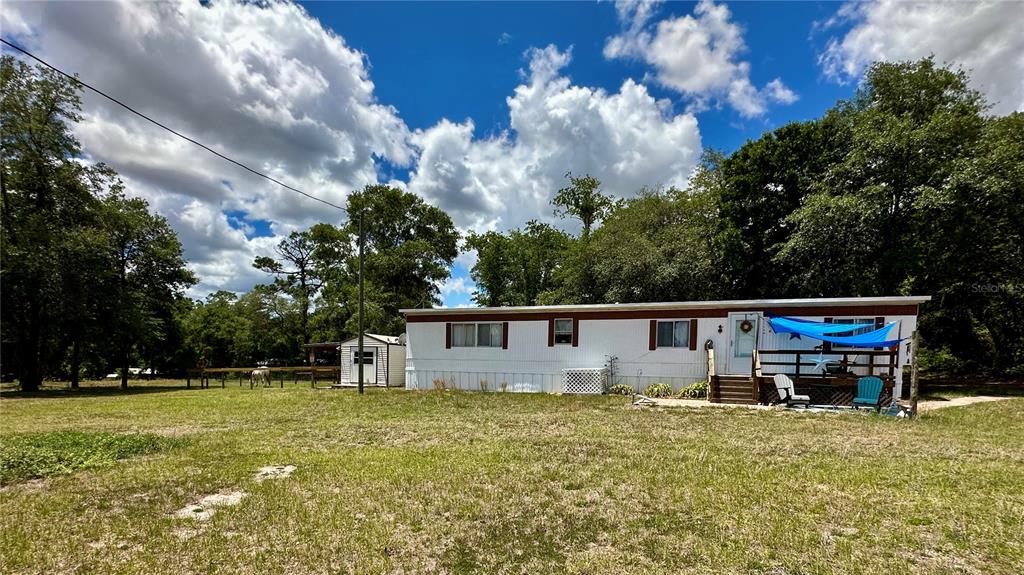 A single-story manufactured home with a shed and a deck sits on a grassy lot — 6250 SE 150TH AVENUE, MORRISTON, FL