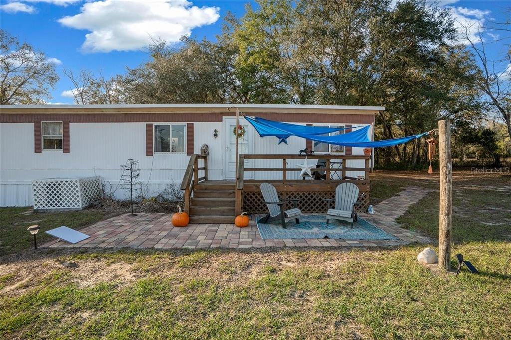 A mobile home features a wooden deck, a brick patio, and a blue shade sail — 6250 SE 150TH AVENUE, MORRISTON, FL