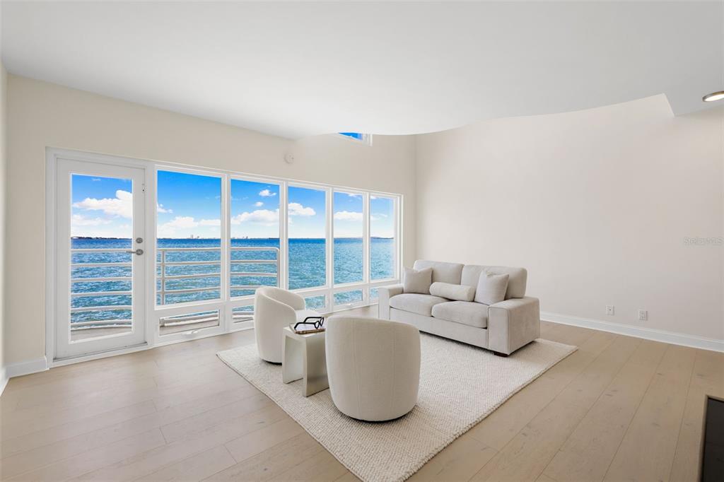 A bright living room features light wood floors, a neutral sofa, and floor-to-ceiling water views — 4950 BAYSHORE BOULEVARD UNIT 23, TAMPA, FL