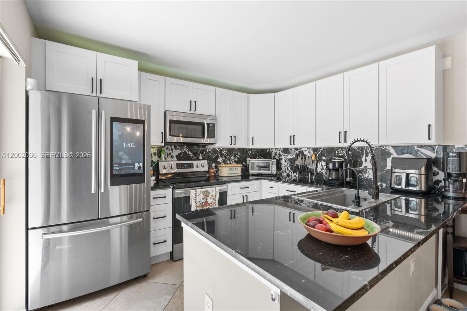A kitchen features white cabinets, black marble-patterned backsplashes, granite countertops, and stainless steel appliances — 7124 71st Way, West Palm Beach FL 33407, WEST PALM BEACH, FL