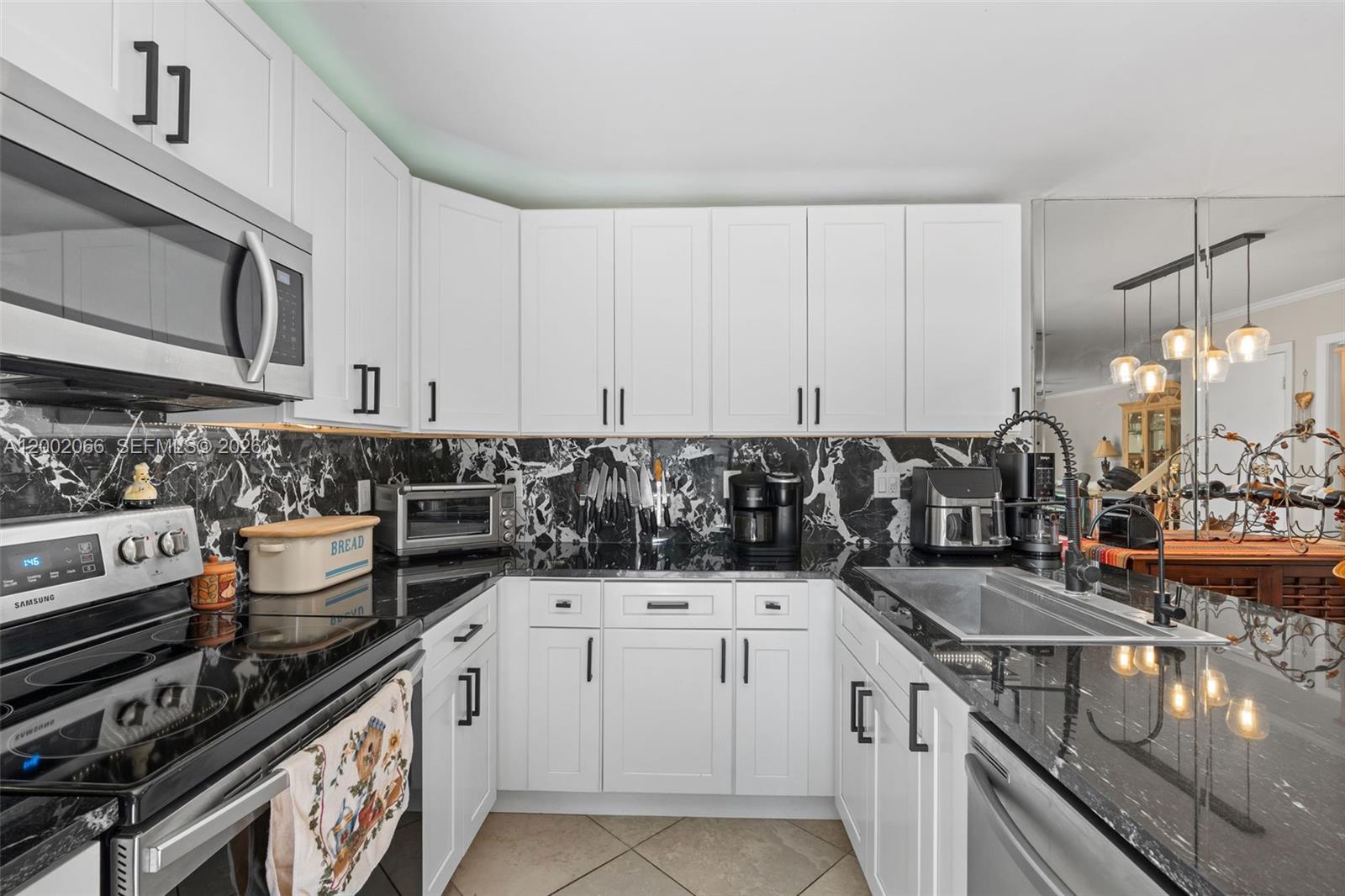 A kitchen features white cabinets, black marble countertops, a black backsplash, and stainless steel appliances — 7124 71st Way, West Palm Beach FL 33407, WEST PALM BEACH, FL