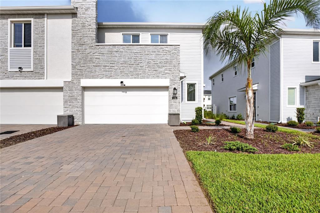 A two-story house exterior features a stone facade, a white garage door, and a paved driveway — 198 NINE IRON DRIVE, CHAMPIONS GATE, FL
