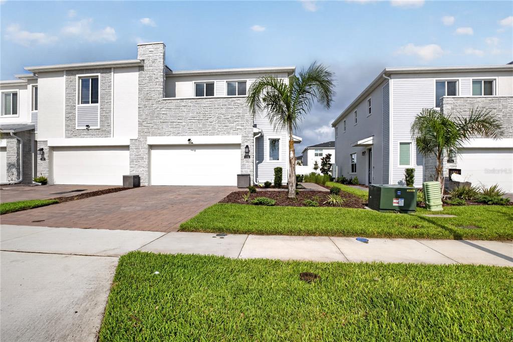 Two modern townhomes with stone facades, white garages, and palm trees under a blue sky — 198 NINE IRON DRIVE, CHAMPIONS GATE, FL