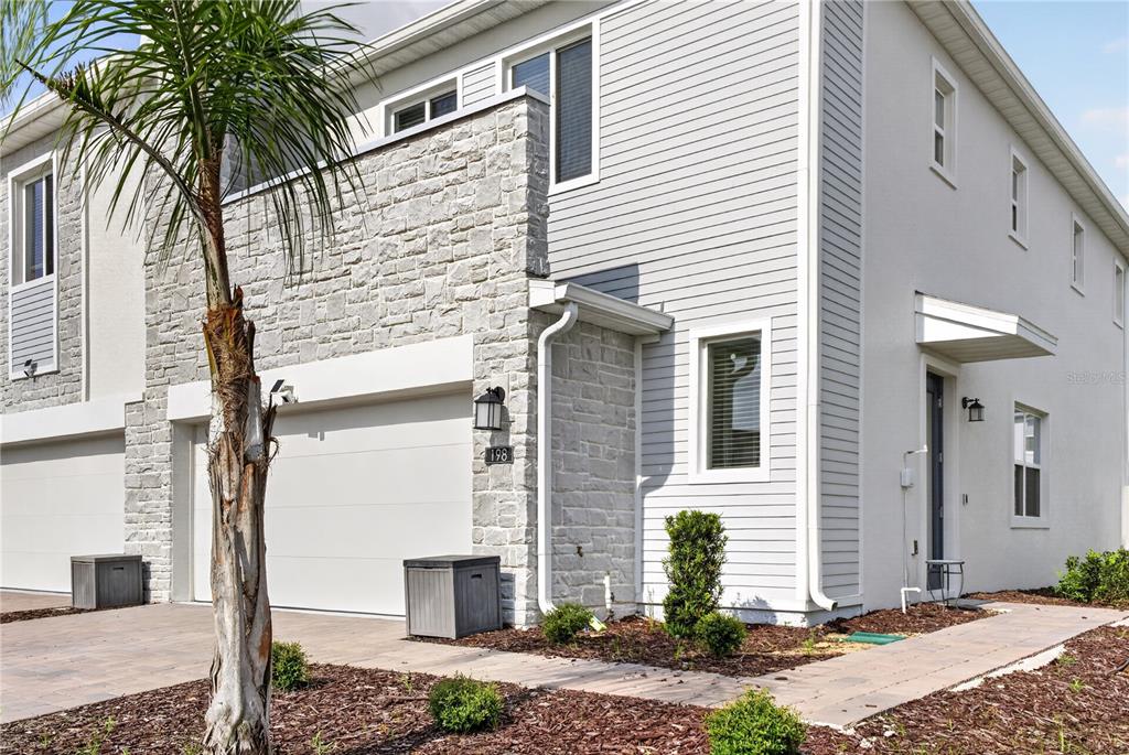 A two-story townhouse exterior features light gray siding, stone veneer accents, and a paved driveway — 198 NINE IRON DRIVE, CHAMPIONS GATE, FL