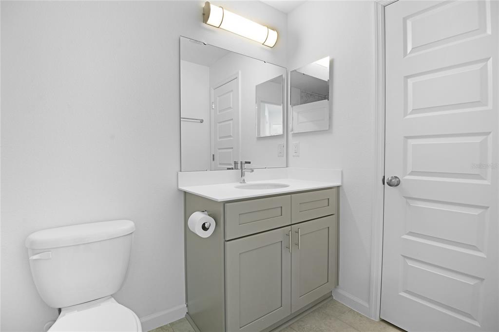 A bathroom features a gray vanity, a white countertop, a mirror, and a toilet — 878 NELSON DRIVE, KISSIMMEE, FL