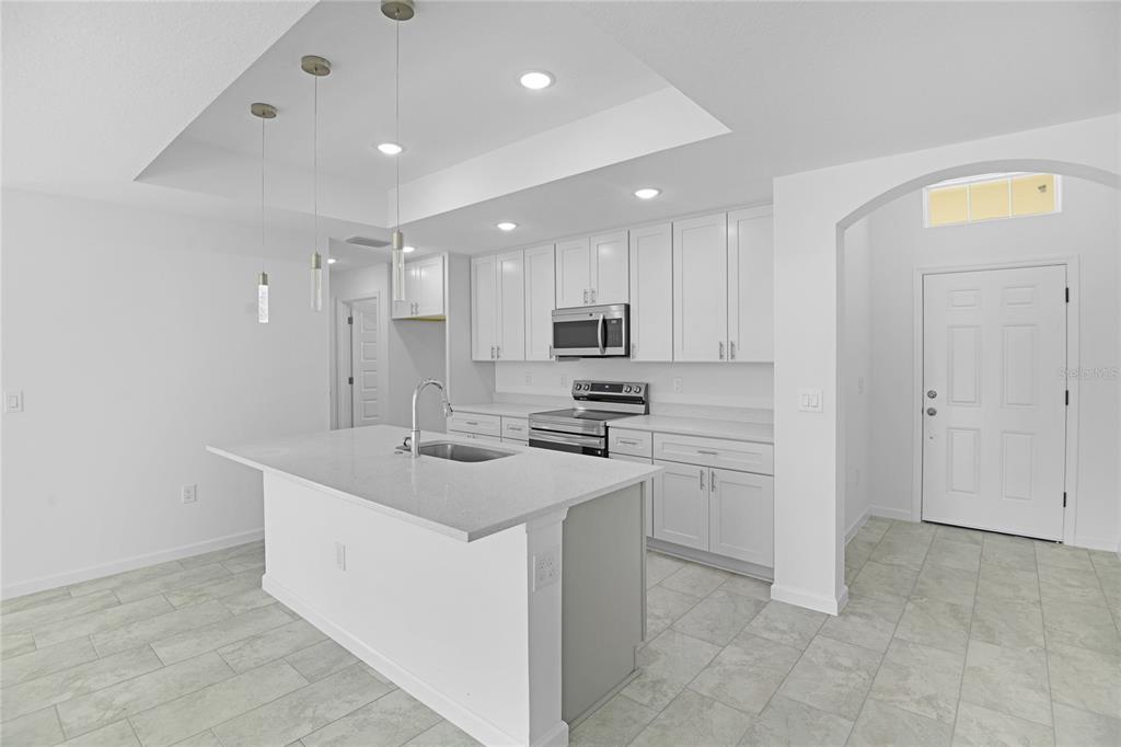 A modern kitchen features white cabinets, a quartz island with a sink, and tile flooring — 878 NELSON DRIVE, KISSIMMEE, FL